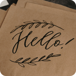 The word 'hello' written in black marker in a decorative script font on brown paper with accompanying rosemary branches curving over the top/bottom in black marker (photo by Cottonbro Studio)