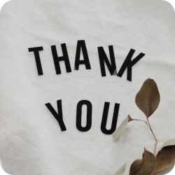 The words 'thank you' written with black plastic marquee letters, placed with loose arrangement on a white cotton sheet with some decorative foliage placed near the letters (photo by Vie Studio)